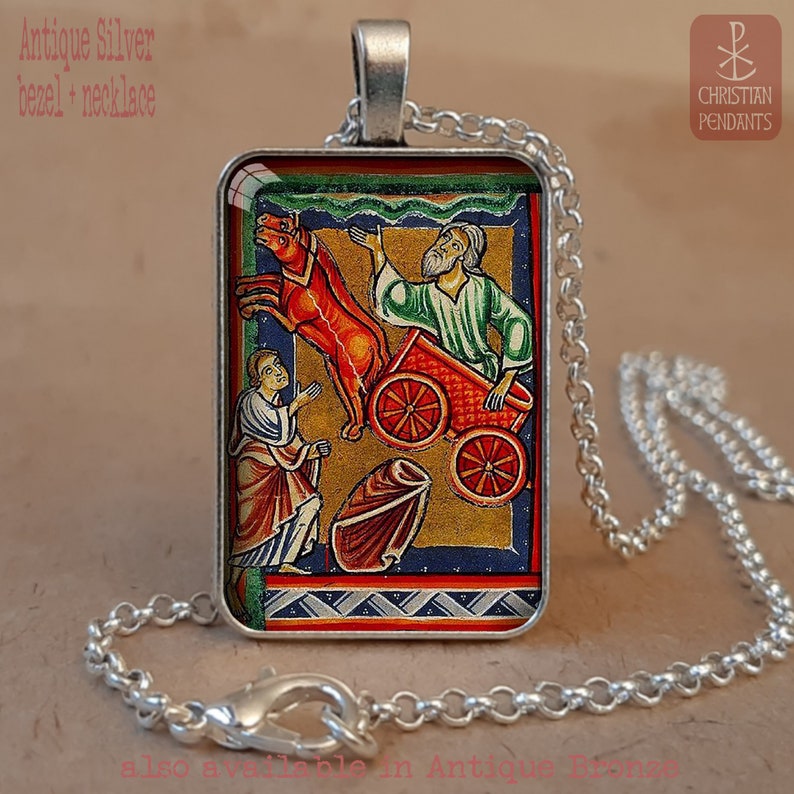 Pode incluir: Colar com pingente retangular de prata antiga. O pingente apresenta uma ilustra&ccedil;&atilde;o medieval colorida com figuras e uma carro&ccedil;a puxada por cavalos. A corrente prateada tem um design de elos e um fecho de lagosta. O texto "Christian Pendants" &eacute; vis&iacute;vel.