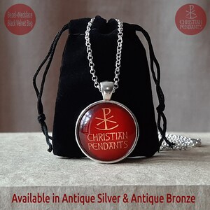 May include: A silver-toned pendant necklace with a red circular pendant featuring a gold Christian symbol and the words "CHRISTIAN PENDANTS." The necklace is displayed with a black velvet bag. Available in antique silver and antique bronze.
