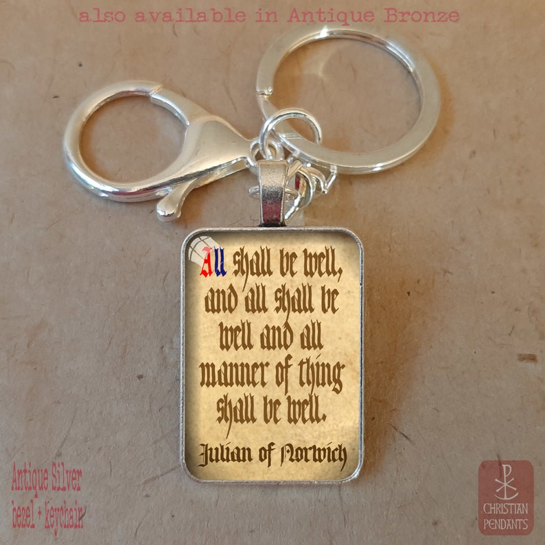 May include: A rectangular silver keychain pendant with the quote "All shall be well" in a vintage font. The keychain includes a lobster clasp and a keyring. The text is in black, red, and blue on a beige background.