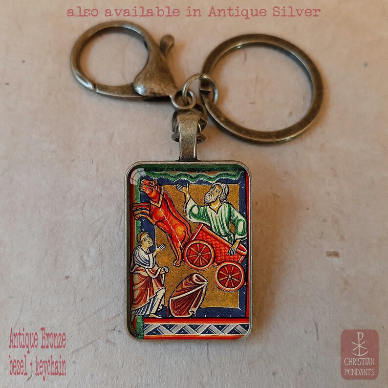 Pode incluir: Porta-chaves em bronze antigo com um pendente retangular com uma ilustra&ccedil;&atilde;o religiosa colorida. O pendente retrata uma cena b&iacute;blica com figuras, uma carro&ccedil;a puxada por cavalos e o texto "Christian Pendants". Tamb&eacute;m dispon&iacute;vel em prata antiga.