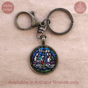 May include: Antique bronze keychain with a round pendant depicting a stained-glass boat scene. The pendant features blue, purple, and green hues. The keychain includes a lobster clasp and a key ring. The text "Available in Antique Bronze only" is visible. The measurements are in cm.