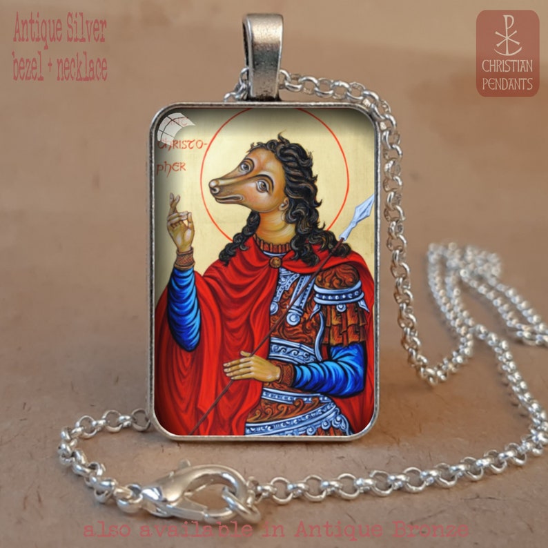 Puede incluir: Collar con colgante de plata antigua. El colgante rectangular presenta una ilustraci&oacute;n de una figura con cabeza de perro, vestida con una capa roja y sosteniendo una lanza. El colgante tiene el texto "CHRISTOPHER". El collar es de cadena de plata.
