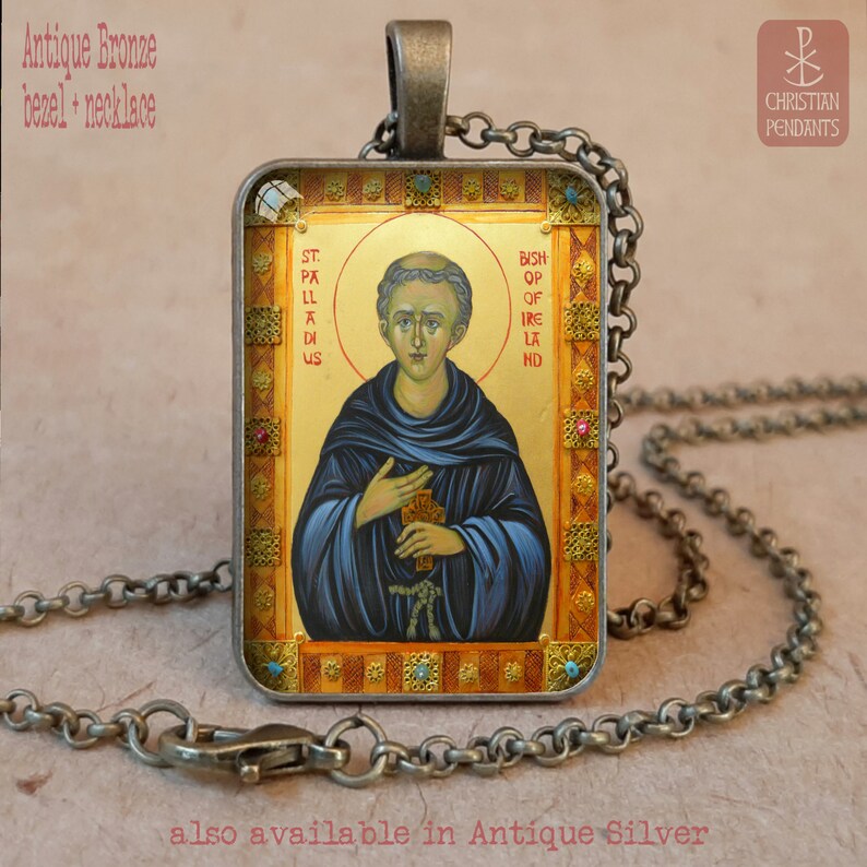 May include: Antique bronze pendant necklace with a religious icon. The rectangular pendant shows a saint with gold details, blue robes, and the text "St. Palladius, Bishop of Ireland." The necklace has a chain and clasp.