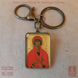 Puede incluir: Llavero de bronce antiguo con un colgante rectangular que presenta un icono religioso en rojo y dorado. El texto "also available in Antique Silver" es visible en la parte superior. El texto "Antique Bronze bezel + keychain" est&aacute; en la parte inferior.