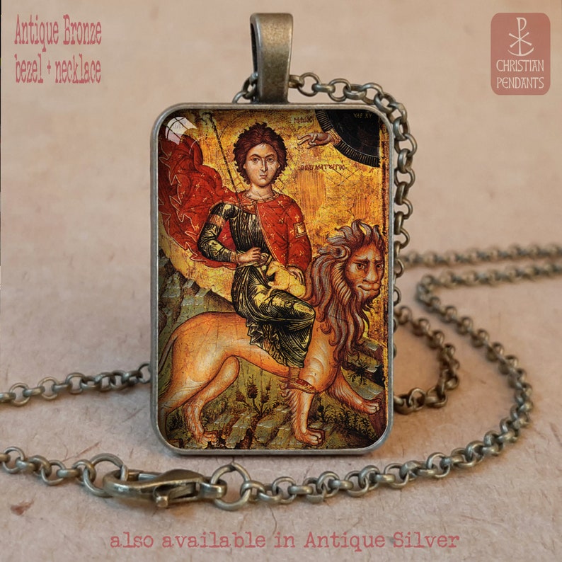 May include: Antique bronze bezel necklace featuring a religious icon. The rectangular pendant displays a figure in red and gold riding a lion. The chain and pendant frame have an antique finish. Text on the image reads "Christian Pendants".