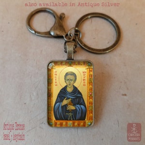 May include: Antique bronze keychain with a rectangular pendant featuring a religious icon. The icon depicts a figure in blue robes holding a cross, with gold text. The keychain has a lobster clasp and a split ring.