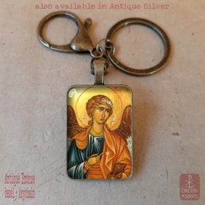 May include: Antique bronze keychain with a rectangular pendant featuring a religious icon. The icon depicts a figure with a golden halo, wings, and a robe. The text "Raphael" is visible. The keychain also available in Antique Silver. Text on the image says "Antique Bronze bezel + keychain".