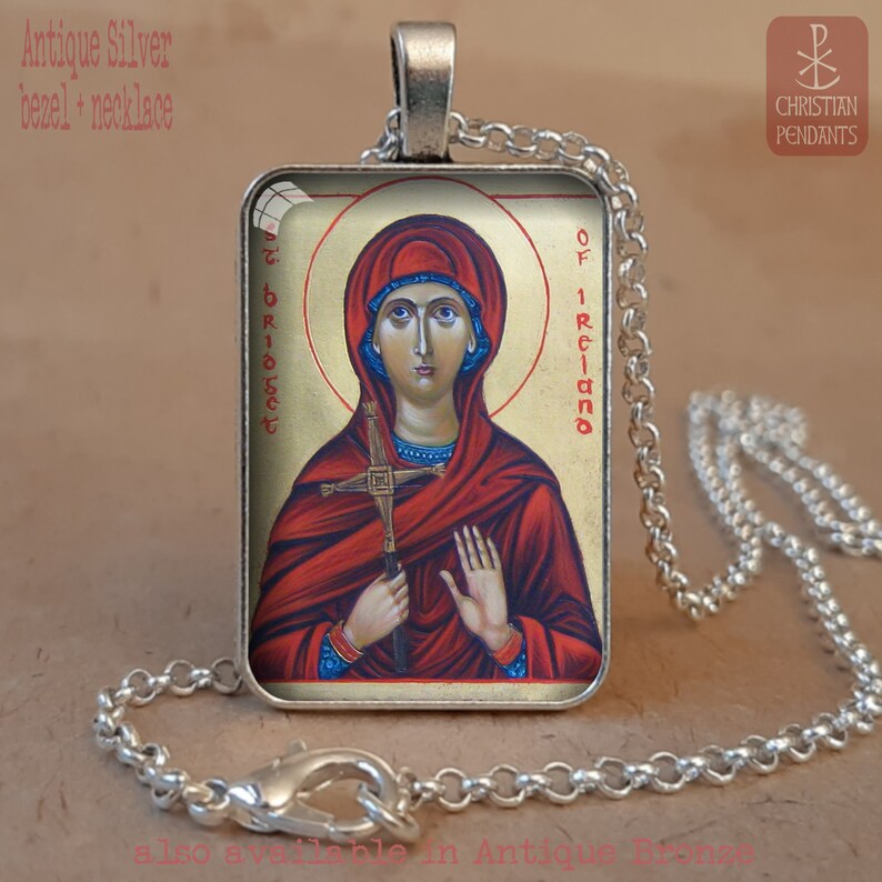 Puede incluir: Collar con colgante de bisel plateado antiguo con un icono religioso de Santa Br&iacute;gida de Irlanda. El colgante rectangular presenta una imagen detallada de la santa en tonos rojos y dorados, sosteniendo una cruz. La cadena del collar es plateada.