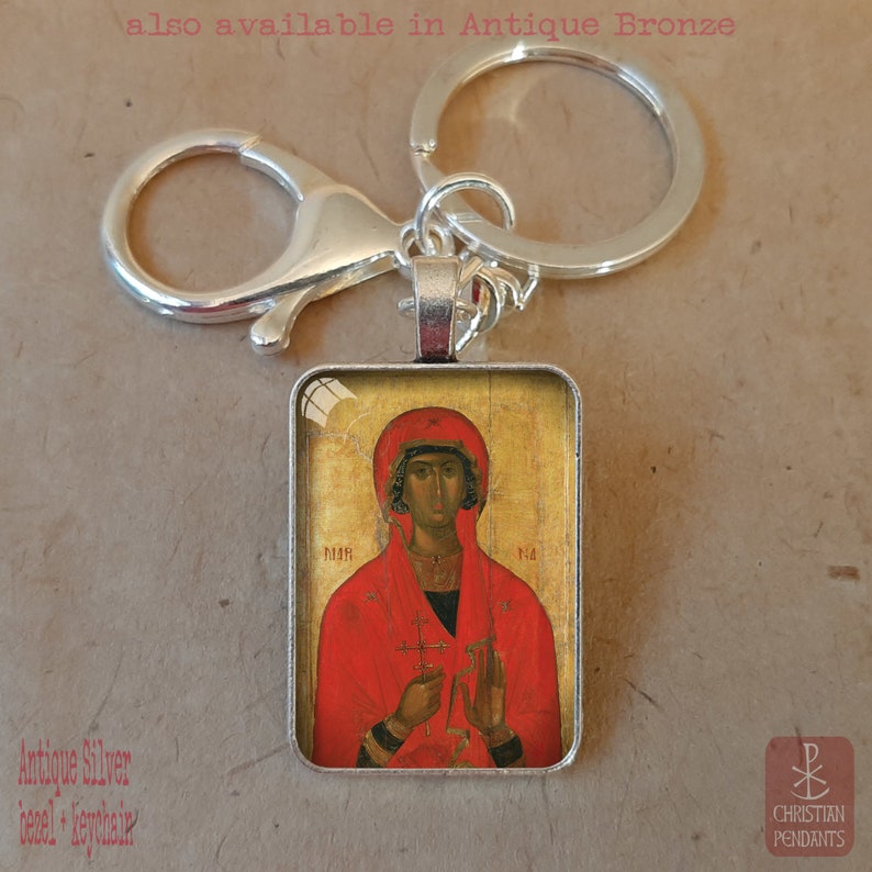 Puede incluir: Llavero con bisel plateado antiguo con un icono religioso. El colgante rectangular muestra una figura con t&uacute;nica y tocado rojos sobre un fondo dorado. El llavero incluye un mosquet&oacute;n y una anilla partida.