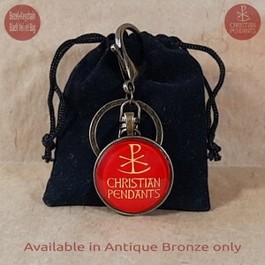 May include: A red Christian pendant keychain with gold lettering and a symbol, attached to a metal clasp and ring. The keychain is presented in a black velvet bag. The text "CHRISTIAN PENDANTS" is visible.