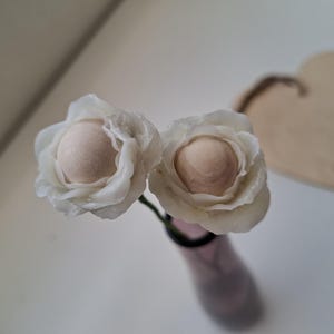 Puede incluir: Dos flores de papel blancas con un centro marrón claro, dispuestas en un jarrón.