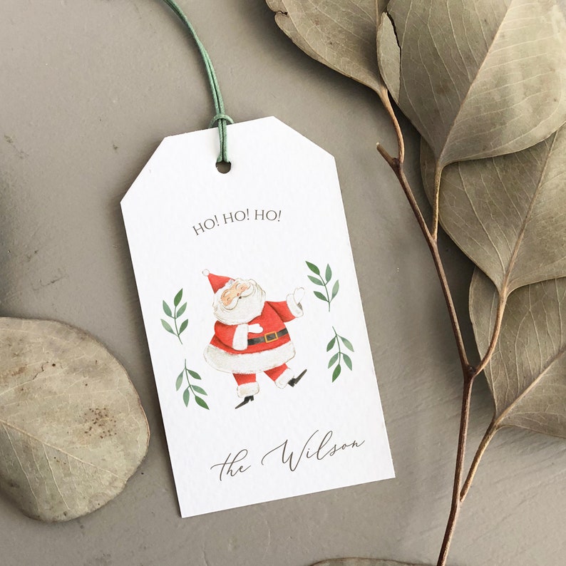 May include: White gift tag with a red and white cartoon Santa Claus illustration, green holly sprigs, and the text "Ho! Ho! Ho!" and "The Wilson".