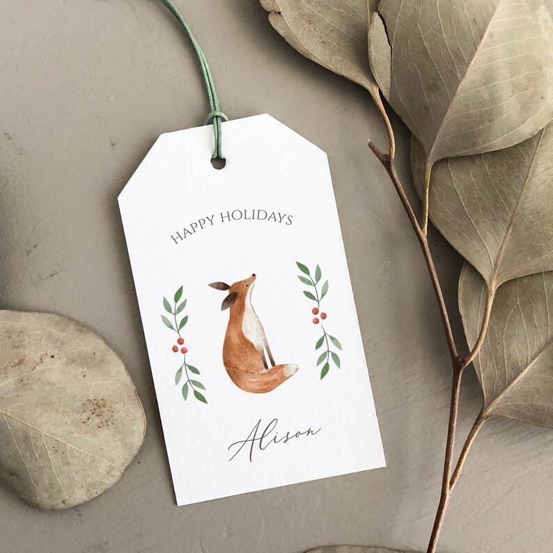 May include: A white gift tag with a green and red holly design and a watercolor illustration of a fox. The tag says "Happy Holidays" and "Alison".