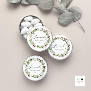 May include: Small, round, silver tins with white lids, each decorated with a watercolour wreath of green leaves and red berries. The lids feature the name "Leonardo" and the text "DOTESSA IN FISICA 2027". One tin is open, revealing white sweets.