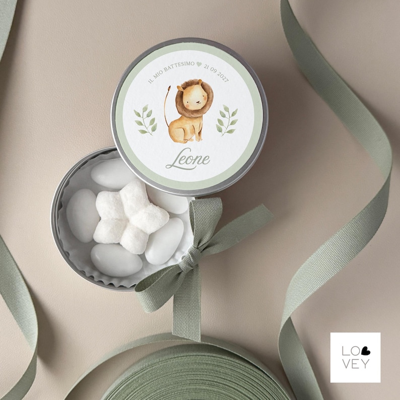 May include: A round, silver tin with a watercolor illustration of a lion cub, text that reads "Il mio battesimo 21 09 2022" and the name "Leone". The tin is open, revealing white candies. A green ribbon and bow are also present.