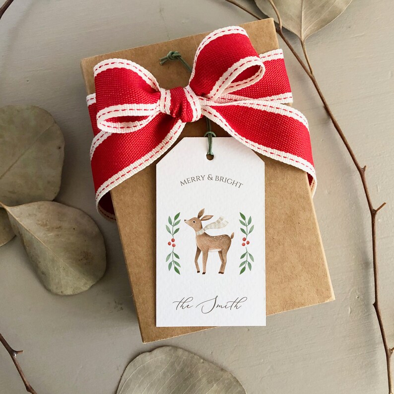 May include: A brown gift box with a red and white striped ribbon bow. A white gift tag with a reindeer illustration and the text "Merry & Bright" and "the Smith" is attached to the box.