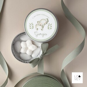 May include: A round, silver tin with a light green lid featuring a watercolor elephant illustration and the name "Giorgia". The tin is open, revealing white candies. A light green ribbon and bow are also present.