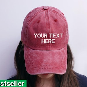 May include: A faded red baseball cap with the text "YOUR TEXT HERE" in white. The cap has a curved peak and a vintage look. The word "Bestseller" is in a green rectangle at the bottom.