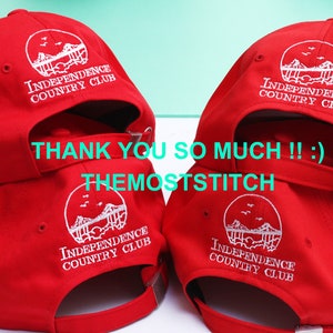 May include: Red baseball caps with white embroidered text and a circular logo that reads "INDEPENDENCE COUNTRY CLUB." The caps have adjustable straps and a curved brim. The text "THANK YOU SO MUCH !! :) THEMOSTSTITCH" is also visible.