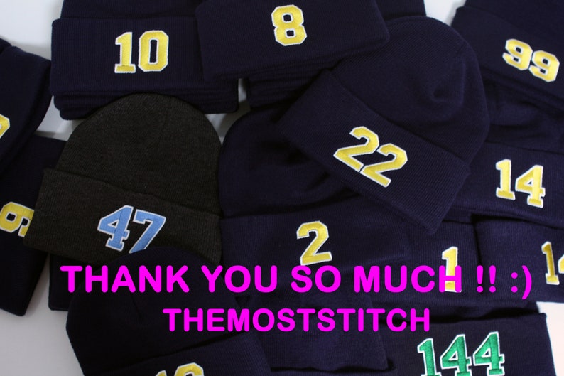 May include: A pile of navy blue knit beanies with various numbers embroidered on them in yellow and light blue. The numbers include 10, 8, 99, 47, 22, 14, 2, 1, and 144. The text "THANK YOU SO MUCH!! :) THEMOSTSTITCH" is visible at the bottom of the image.