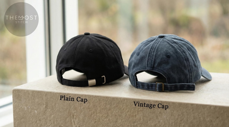Puede incluir: Dos gorras de b&eacute;isbol, una negra y otra azul descolorida, se muestran juntas. La gorra negra tiene una hebilla plateada, y la azul una hebilla bronce. El texto "Plain Cap" y "Vintage Cap" est&aacute; debajo.