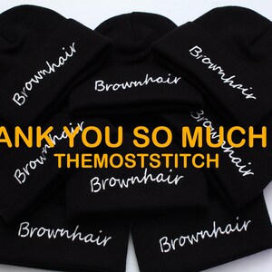 May include: A stack of black beanies with white embroidered text that reads "Brownhair" and "THEMOSTSTITCH".