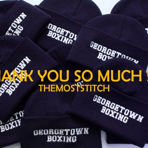 May include: A pile of navy blue knit beanies with white embroidered text that reads "Georgetown Boxing" and "Town NG". The text "Thank You So Much!! :) TheMostStitch" is visible in the image.