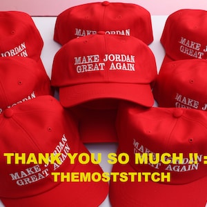 May include: A collection of red baseball caps with white embroidered text. The text on the caps reads "MAKE JORDAN GREAT AGAIN". The caps are arranged in a group, with some overlapping. The image also includes the text "THANK YOU SO MUCH IN:) THEMOSTSTITCH".