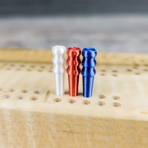 May include: Three wooden game pieces in red, white, and blue, standing upright on a wooden game board. The board has a grid of holes.