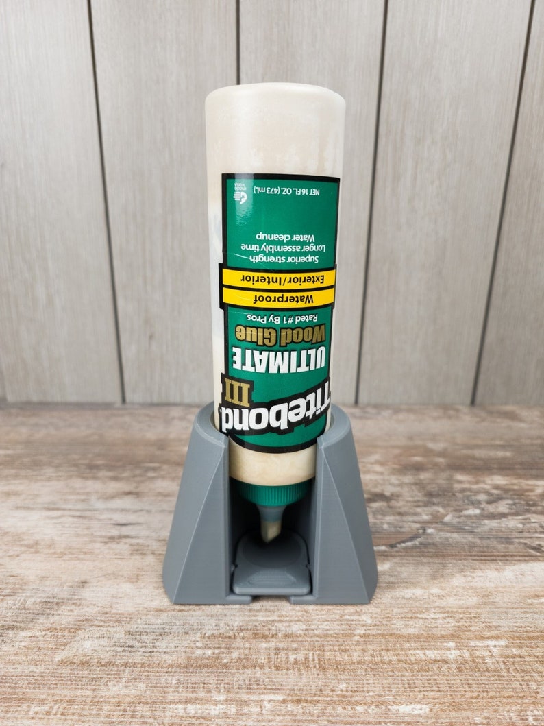May include: A white bottle of Titebond Ultimate III Wood Glue, a waterproof adhesive rated #1 by professionals, is displayed in a grey plastic dispenser. The bottle is labelled with the product name, its features, and net volume of 473 ml (16 fluid ounces).