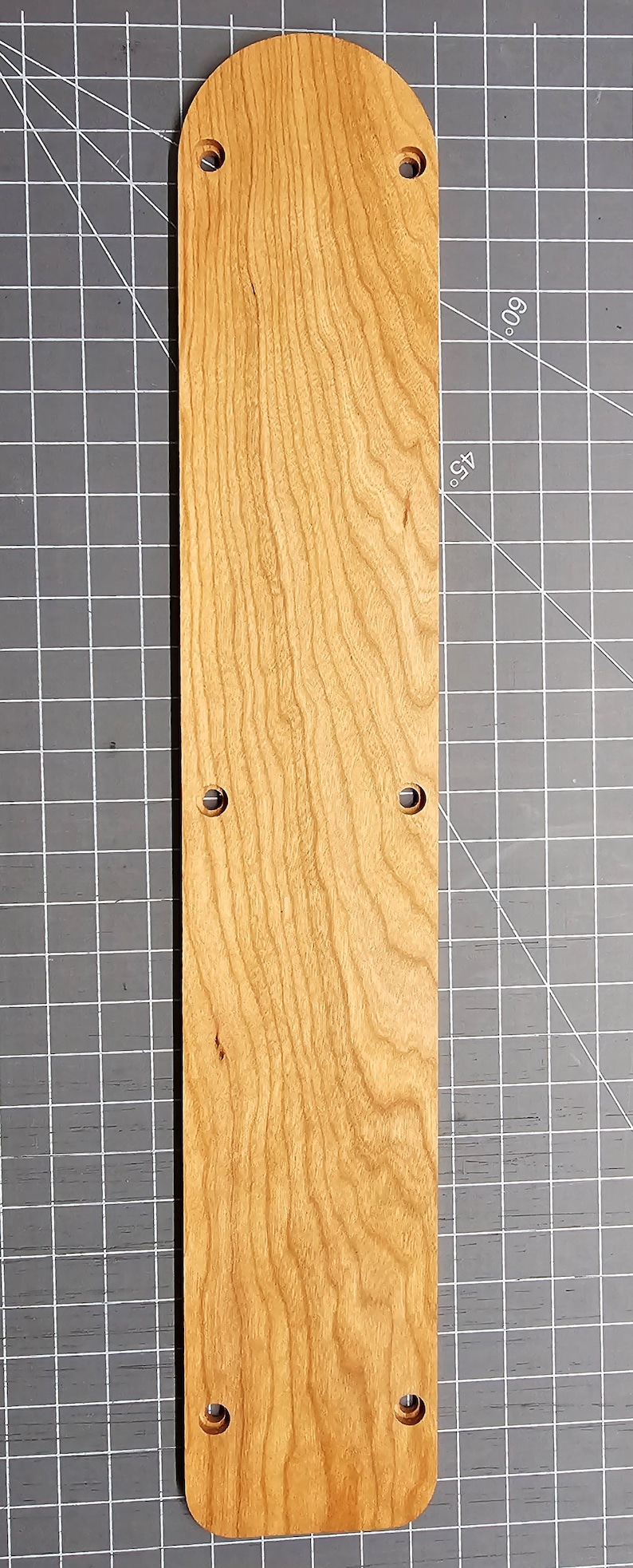 May include: A long, narrow, rectangular wooden plaque with a rounded top and a natural wood finish. The plaque has six evenly spaced holes drilled into it.