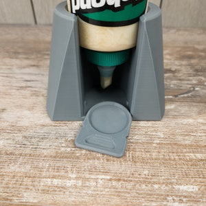 May include: Grey 3D printed glue bottle holder with a removable lid. The holder is designed to hold a bottle of Titebond III wood glue.