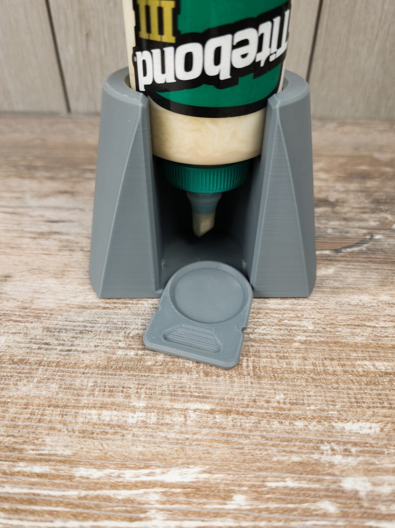 May include: Grey 3D printed glue bottle holder with a removable lid. The holder is designed to hold a bottle of Titebond III wood glue.