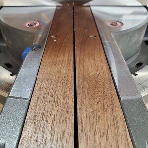 Puede incluir: Primer plano de una sierra de mesa de madera con una superficie de madera marr&oacute;n oscura y un protector de hoja de metal plateado.