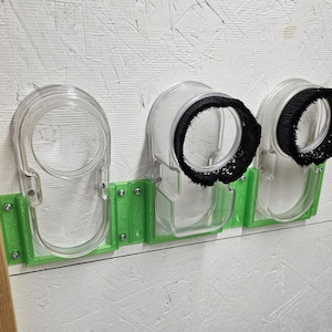 May include: Three clear plastic wall-mounted storage containers with black brush attachments. The containers are mounted on green plastic brackets.