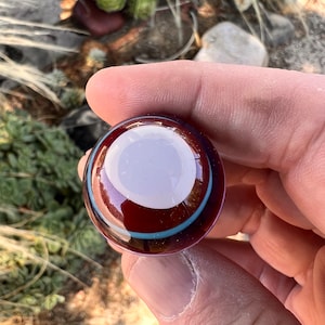 May include: A round glass marble with a white center and concentric rings of red, blue, and white.