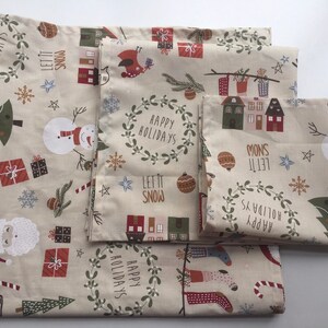 以下が含まれることがあります： ベージュの背景に、クリスマスをテーマにした布のセット。雪だるま、サンタクロース、プレゼント、「Happy Holidays」と「Let it Snow」などのホリデーモチーフが特徴です。さまざまなサイズの布です。