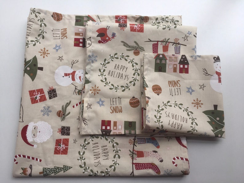 以下が含まれることがあります： ベージュの背景に、クリスマスをテーマにした布のセット。雪だるま、サンタクロース、プレゼント、「Happy Holidays」と「Let it Snow」などのホリデーモチーフが特徴です。さまざまなサイズの布です。