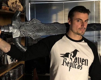 May include: A large, silver-colored fantasy sword with intricate geometric engravings on the blade and hilt, held horizontally across the shoulders. The sword features a dark, weathered metallic finish and a long, straight, double-edged blade.