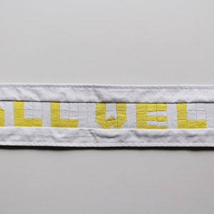 May include: A white fabric banner with the word "ALL WELL" spelled out in yellow squares.