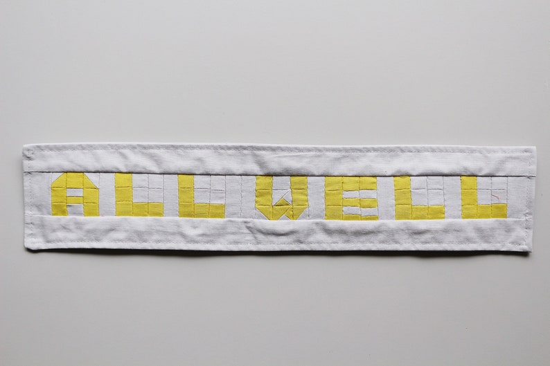 May include: A white fabric banner with the word "ALL WELL" spelled out in yellow squares.