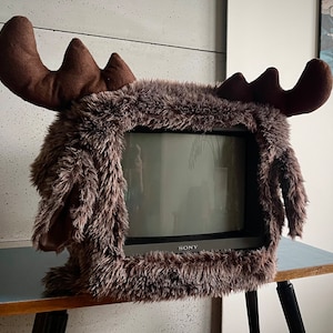 May include: A vintage television set with a brown faux fur moose head cover. The television screen is black and white and the television is labelled "SONY".