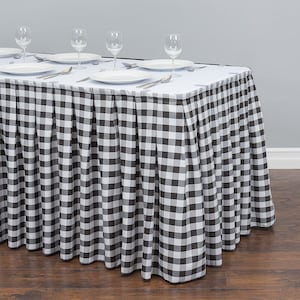 May include: Black and white checkered table skirt with pleats. The skirt is draped over a white tablecloth with four place settings.