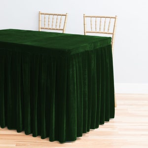 May include: A dark green velvet table cover with pleated skirting. The rectangular table is set in front of two light-colored wooden chairs. The table cover is a solid color and has a soft, luxurious appearance.
