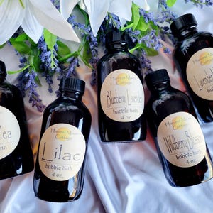 May include: Five amber glass bottles with labels that say "Harvest Moon Cottage" and different scents: Sweet Pea, Lilac, Blueberry Lavender, Wildberry Blossom, and Lavender Marshmallow. Each bottle contains 4 ounces of bubble bath.