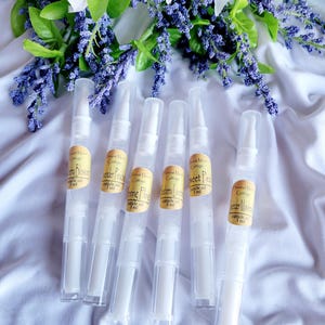 May include: Six clear plastic tubes with white labels. The labels have the text "Harvest Moon Cottage" and different scents: "Sweet Pea", "Lavender Peach", "Morning Glory", "Blueberry Blossom", "Sweet Pea", and "Butter Meadow". Each tube contains 3 ml of cuticle oil.