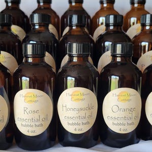 May include: A collection of amber glass bottles with black caps, each labeled with essential oil names like Rose, Lavender, and Orange. The labels are oval-shaped with a logo and the words "bubble bath" and "4 oz."