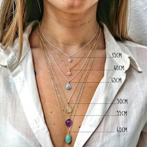 May include: A collection of layered necklaces with gemstone pendants in various colors, including pink, blue, and purple. The necklaces are displayed at different lengths, ranging from 35cm to 60cm, showcasing the different lengths available.