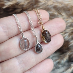 May include: Three gemstone pendant necklaces. The pendants are oval and round, with black inclusions in a clear stone. One necklace has a gold chain and pendant setting, while the other two have silver chains and settings.