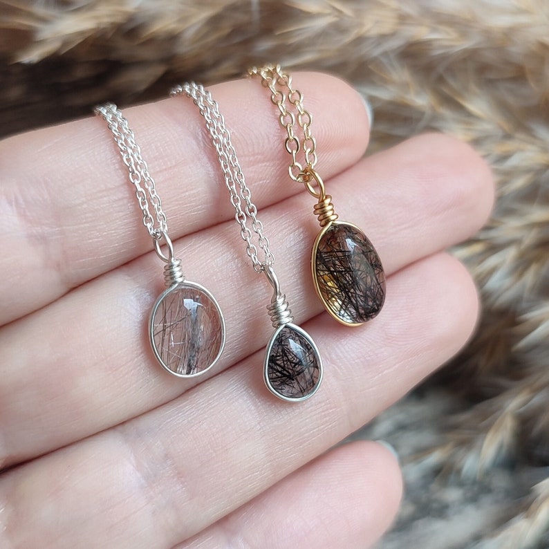 May include: Three gemstone pendant necklaces. The pendants are oval and round, with black inclusions in a clear stone. One necklace has a gold chain and pendant setting, while the other two have silver chains and settings.